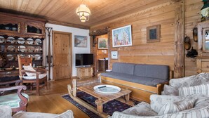 A cozy wooden cabin interior with a sofa, chairs, a television, and a collection of dishes on shelves. - Cozy 3-bedroom apartment near Megève center, balcony, fireplace, sleeps 8 (Megève)