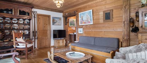 A cozy wooden cabin interior with a sofa, chairs, a television, and a collection of dishes on shelves.