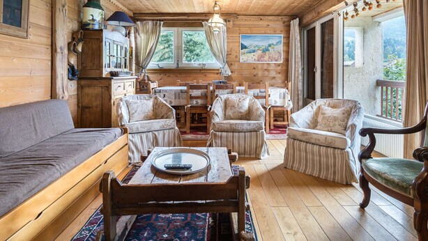 A cozy cabin interior with a wooden ceiling, a sofa, a dining table with chairs, and a view through the windows. - Cozy 3-bedroom apartment near Megève center, balcony, fireplace, sleeps 8 (Megève)