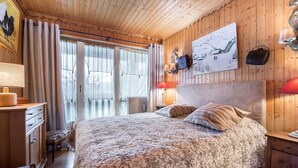A wooden-paneled bedroom with a large bed, a dresser, a chair, and a window with curtains. - Cozy 3-bedroom apartment near Megève center, balcony, fireplace, sleeps 8 (Megève)