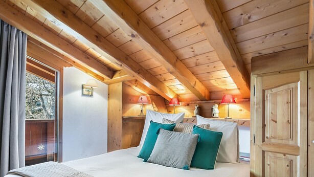 A wooden cabin bedroom with a bed, pillows, a nightstand, and a lamp.
