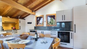 A modern kitchen with wooden beams, a dining table set for four, and a view of the outdoors through a window.