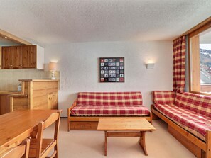 A cozy room with a wooden table, bench, and sofa, a kitchen area, and a wall with a framed picture.