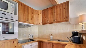 A compact kitchen with wooden cabinets, a built-in microwave, a dishwasher, and a coffee maker. - Charming 2-Room, South Balcony, Ski-In/Ski-Out (Méribel)