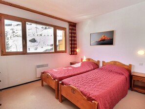 A room with two wooden beds, a window with a view of a snowy landscape, a painting on the wall, and a heater.
