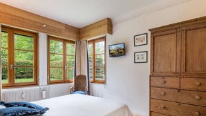 A bedroom with a bed, a wooden wardrobe, and large windows with curtains.
