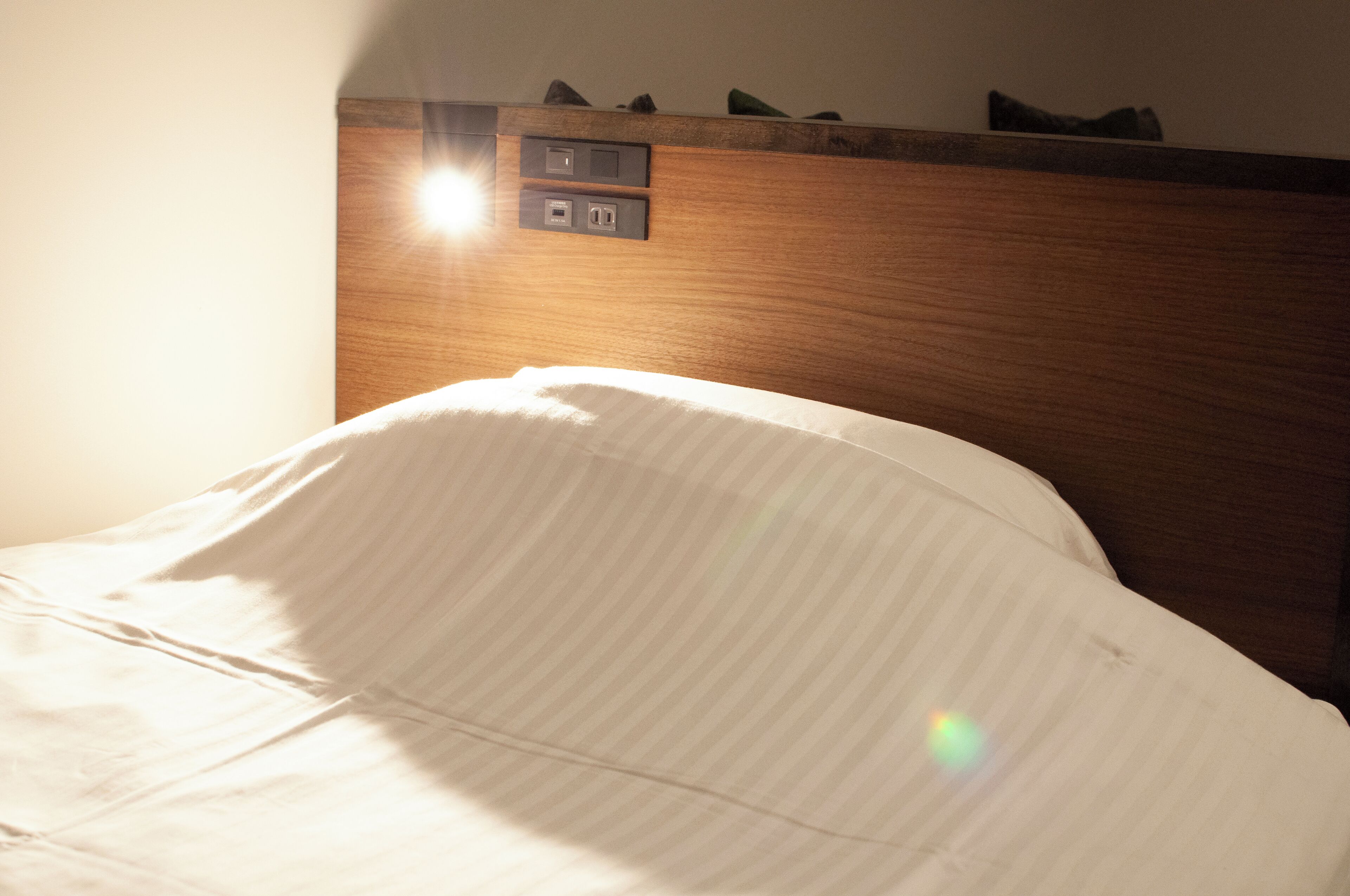 A hotel room with a wooden headboard, a bed with white bedding, and a control panel above the headboard.