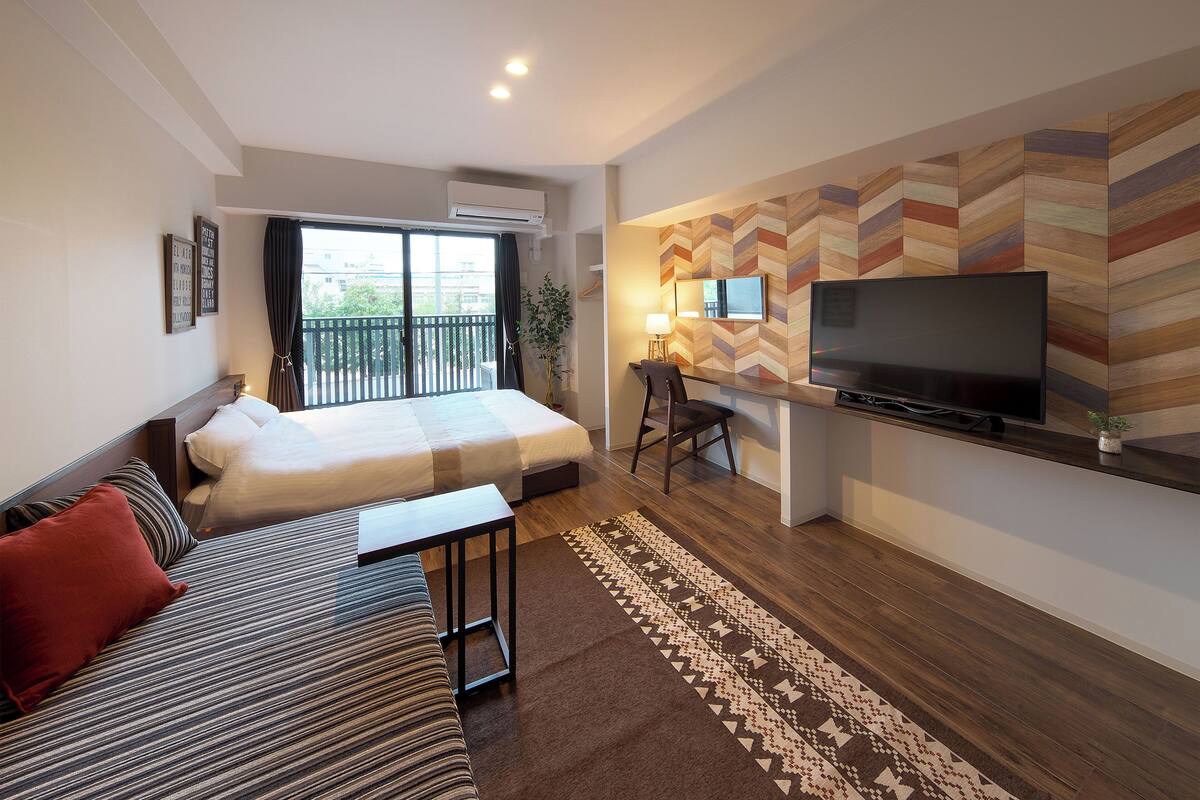 A modern hotel room with a large bed, a sofa, a TV, and a desk.