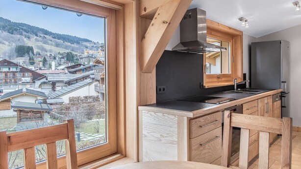 A modern kitchen with a large window, wooden cabinetry, and a view of a town.