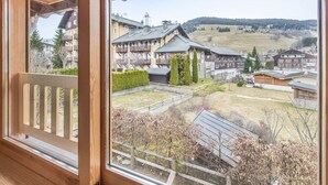 A view from a window of a building with a wooden balcony, overlooking a residential area with houses and a hilly landscape.
