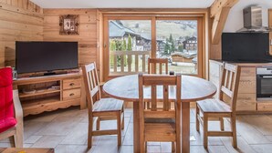 A wooden interior with a dining table, chairs, a TV, and a kitchen area with a view of a snowy landscape.