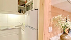 Una cocina con armarios blancos, un refrigerador y una pared de madera.