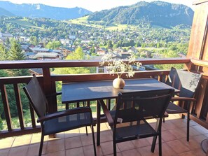 Un balcon avec une table et des chaises, donnant sur une ville et des montagnes.