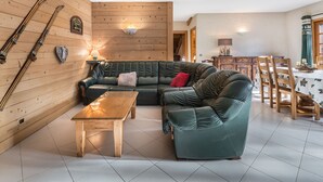 A cozy living room with a green leather sofa, a wooden coffee table, and skis mounted on the wall. - 2-Bedroom Apartment in Megève Center with WiFi (Megève)