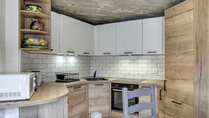 A compact kitchen with white cabinets, a wooden countertop, a built-in oven, and a microwave. - 2-Bedroom Apartment in Megève Center with WiFi (Megève)