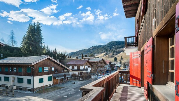 A wooden balcony overlooking a street with traditional buildings, a clear sky, and a mountainous backdrop. - 2-Bedroom Apartment in Megève Center with WiFi (Megève)