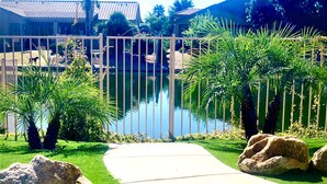 Área ajardinada com um caminho que leva a uma piscina, cercada por palmeiras e pedras.