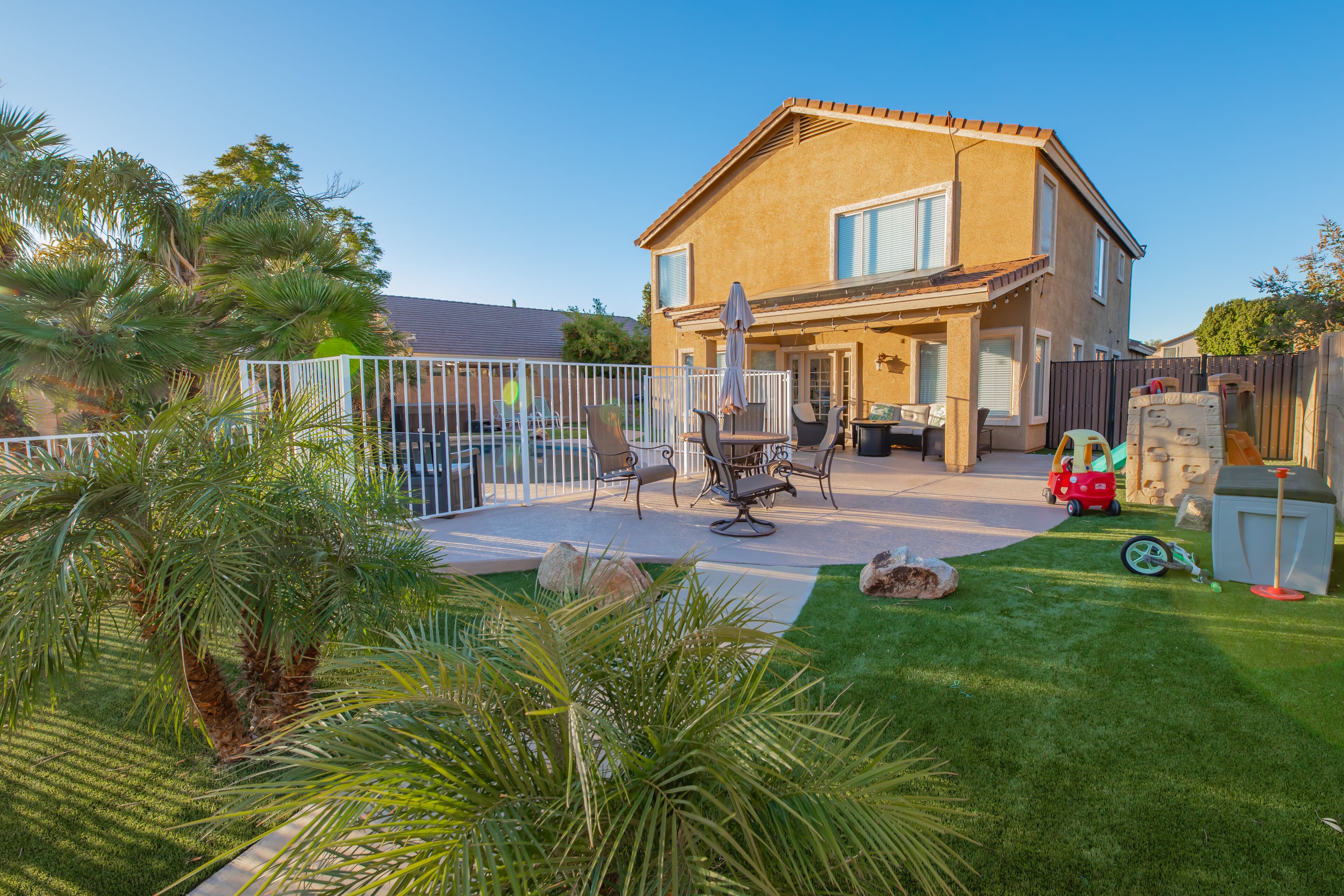 Une maison à deux étages avec un patio, du mobilier d’extérieur et une cour clôturée.