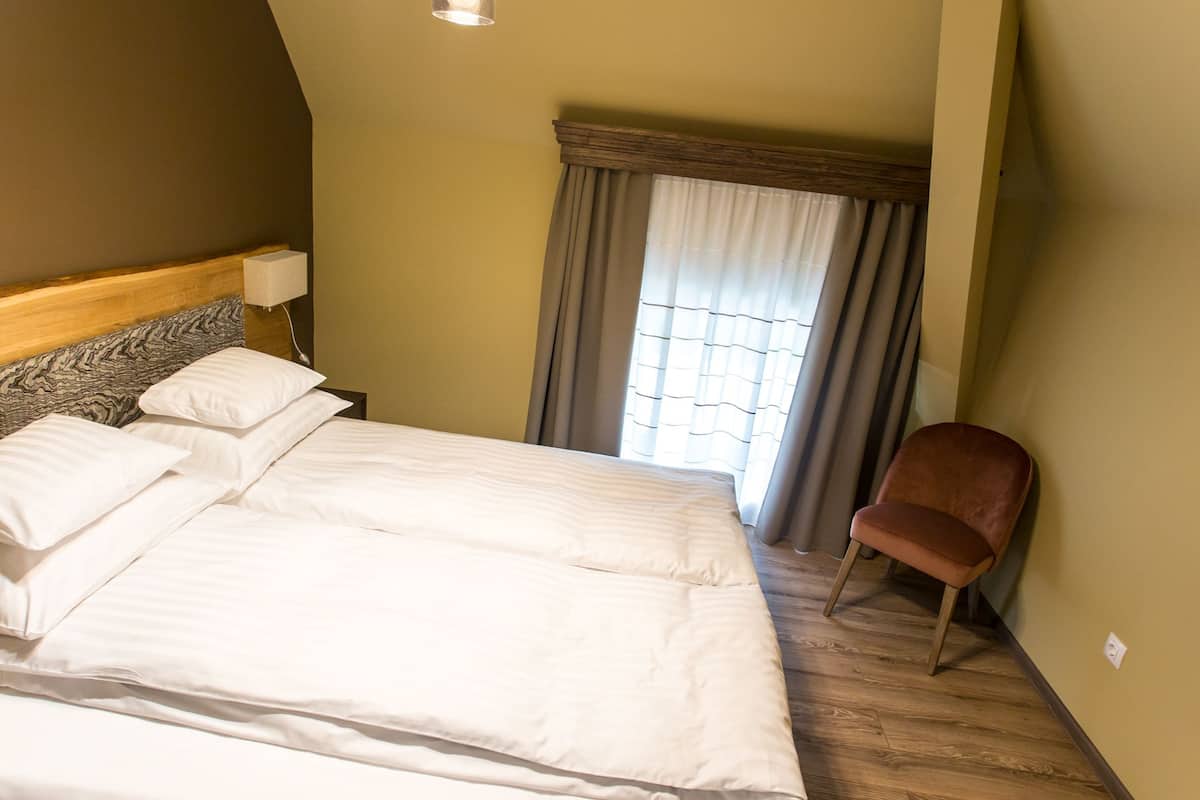 Een hotelkamer met een groot bed, een houten hoofdeinde, een stoel en een raam met gordijnen.