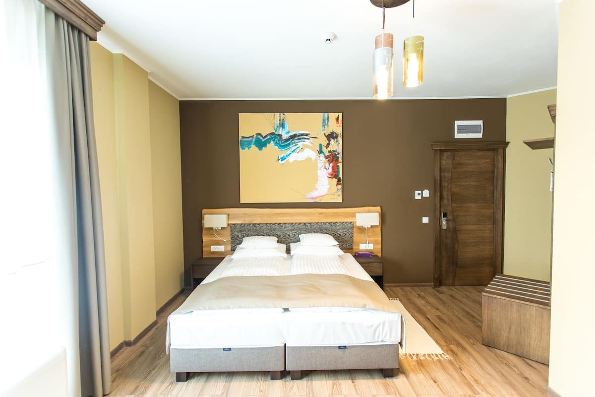 Een hotelkamer met een bed, een houten hoofdeinde, een schilderij aan de muur en een houten kledingkast.