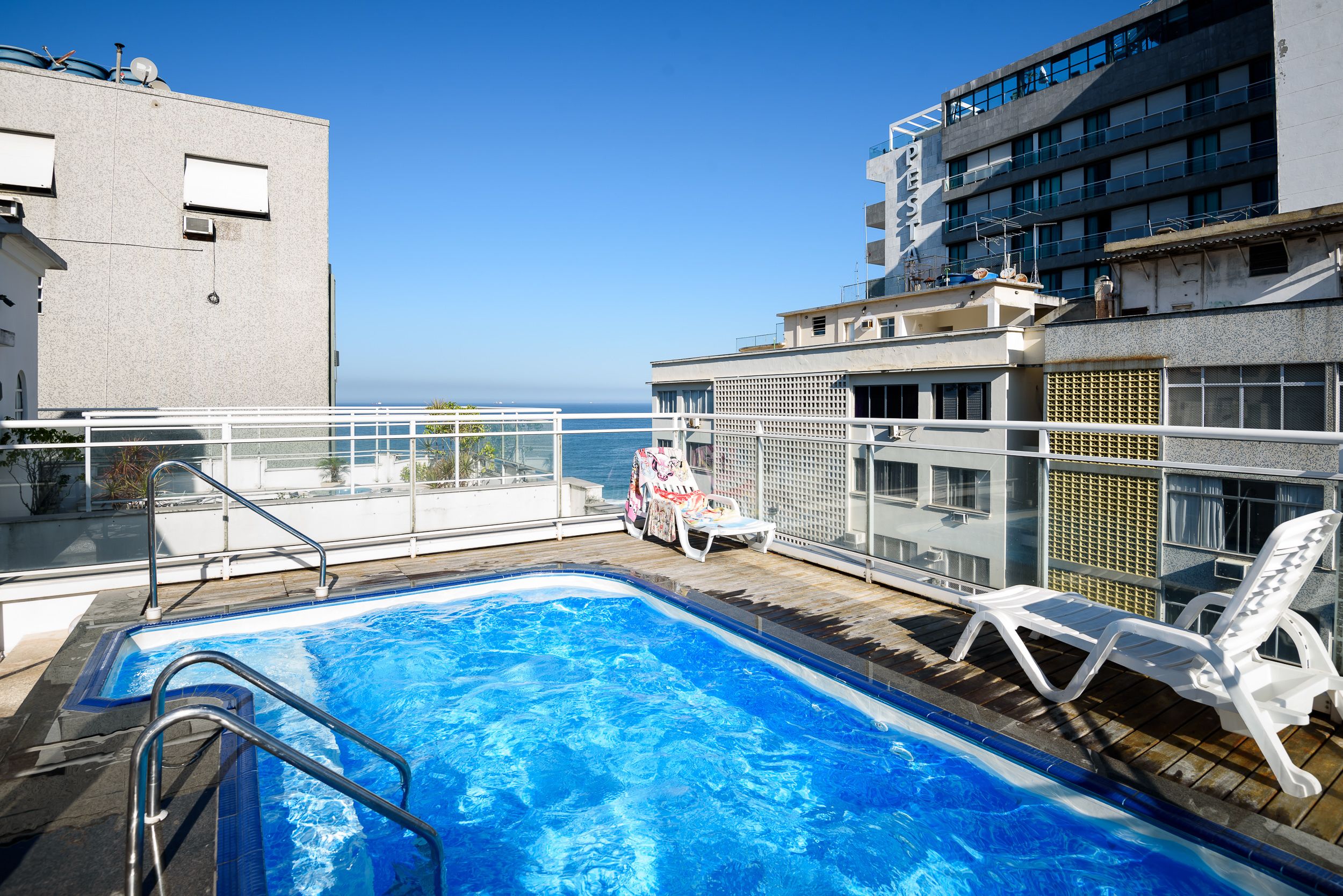A rooftop swimming pool with a view of the ocean, surrounded by buildings.