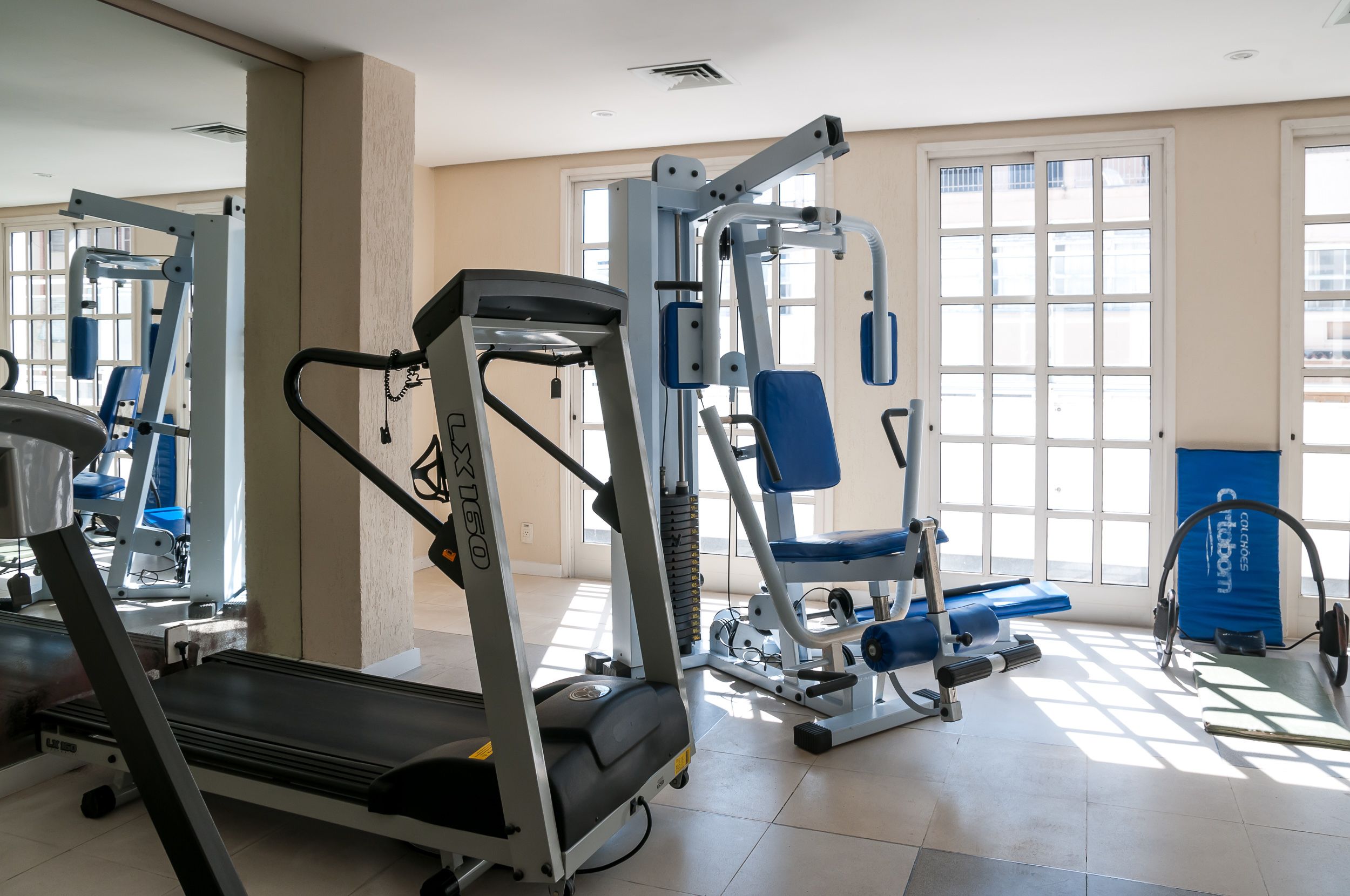 Une salle de sport équipée de machines de cardio, d’appareils de musculation et de grandes fenêtres laissant entrer la lumière naturelle.