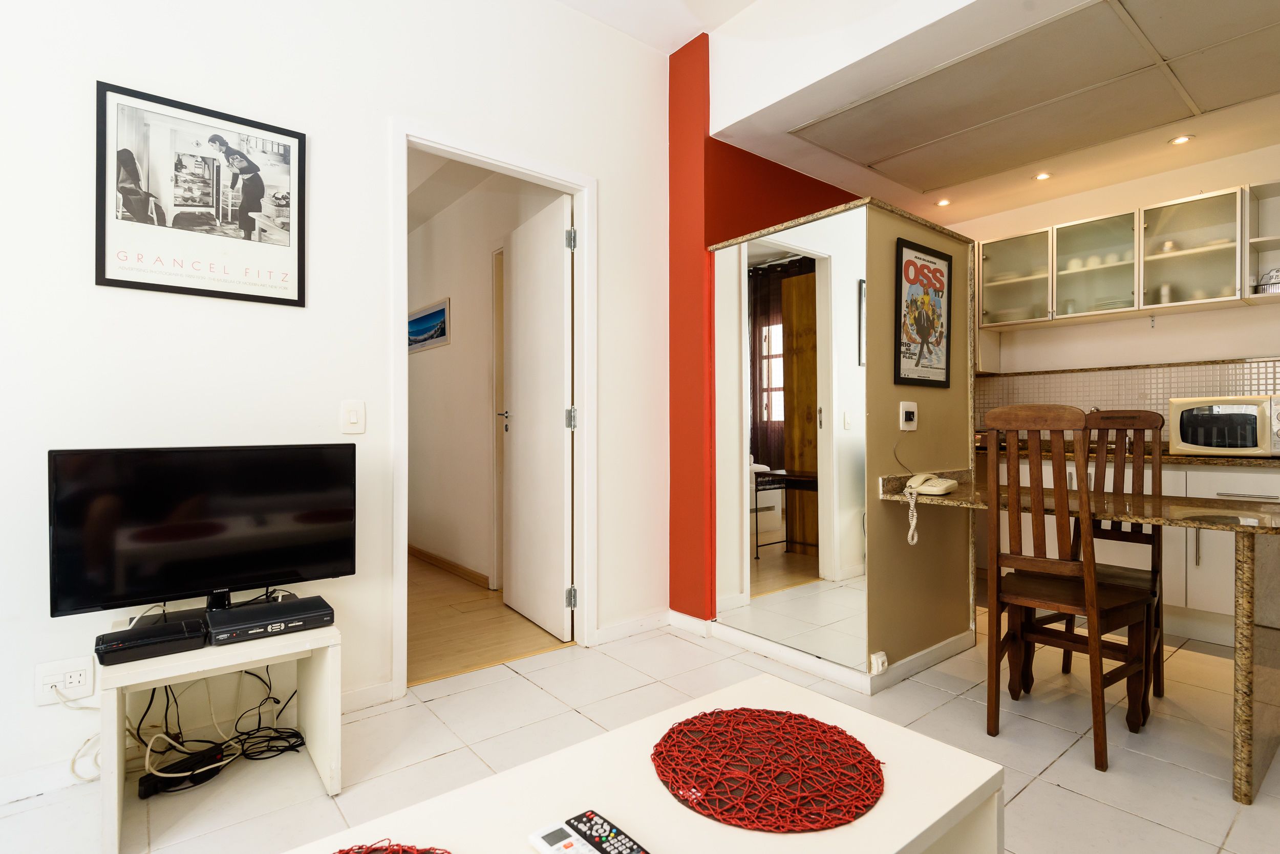 A living room with a flat-screen TV, a coffee table, and a dining area with a chair and table.