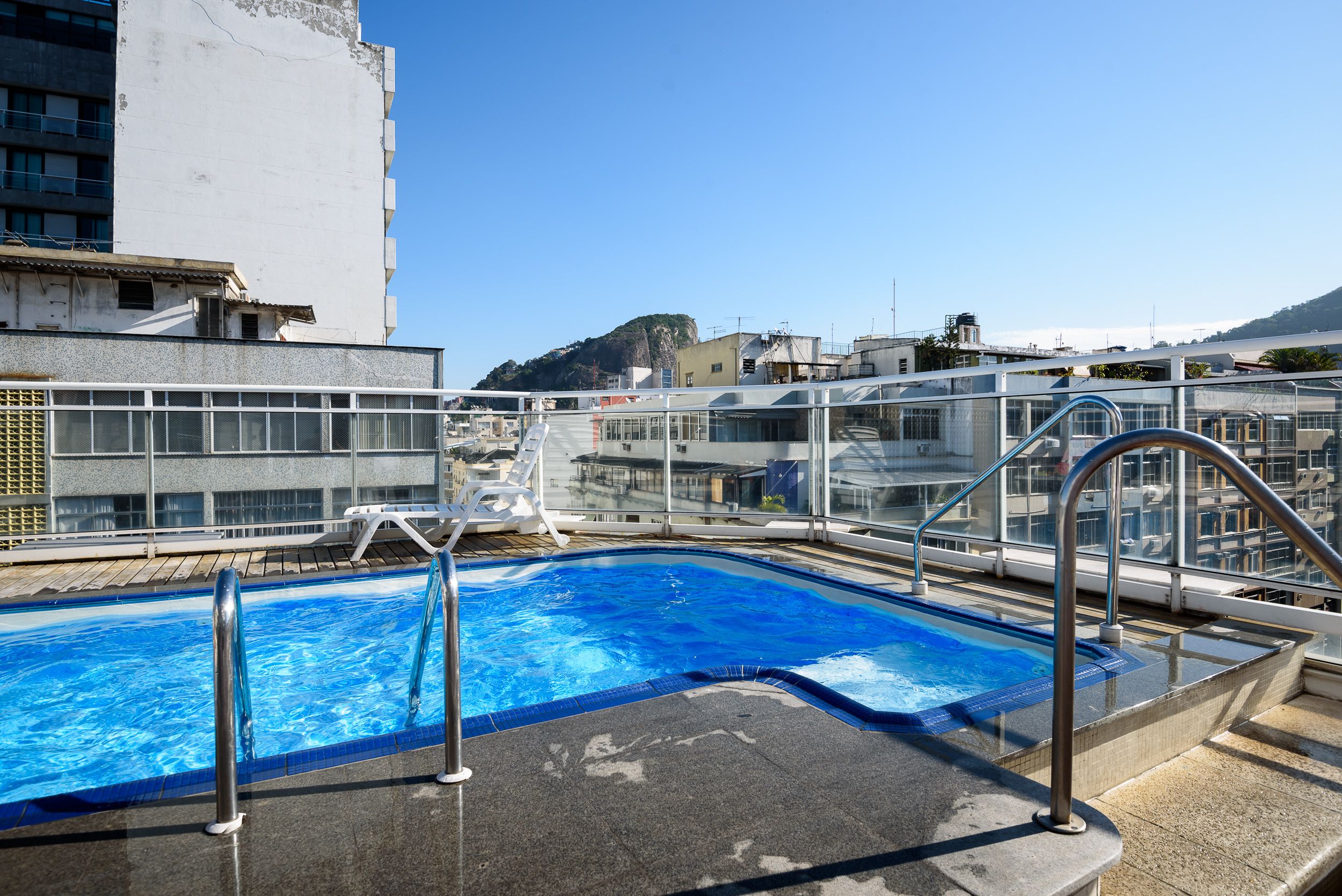 A rooftop pool with clear blue water, surrounded by glass railings and metal handrails.