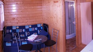 Interior de una cabaña de madera con sofá, dos sillones, una mesita y zona de ducha.