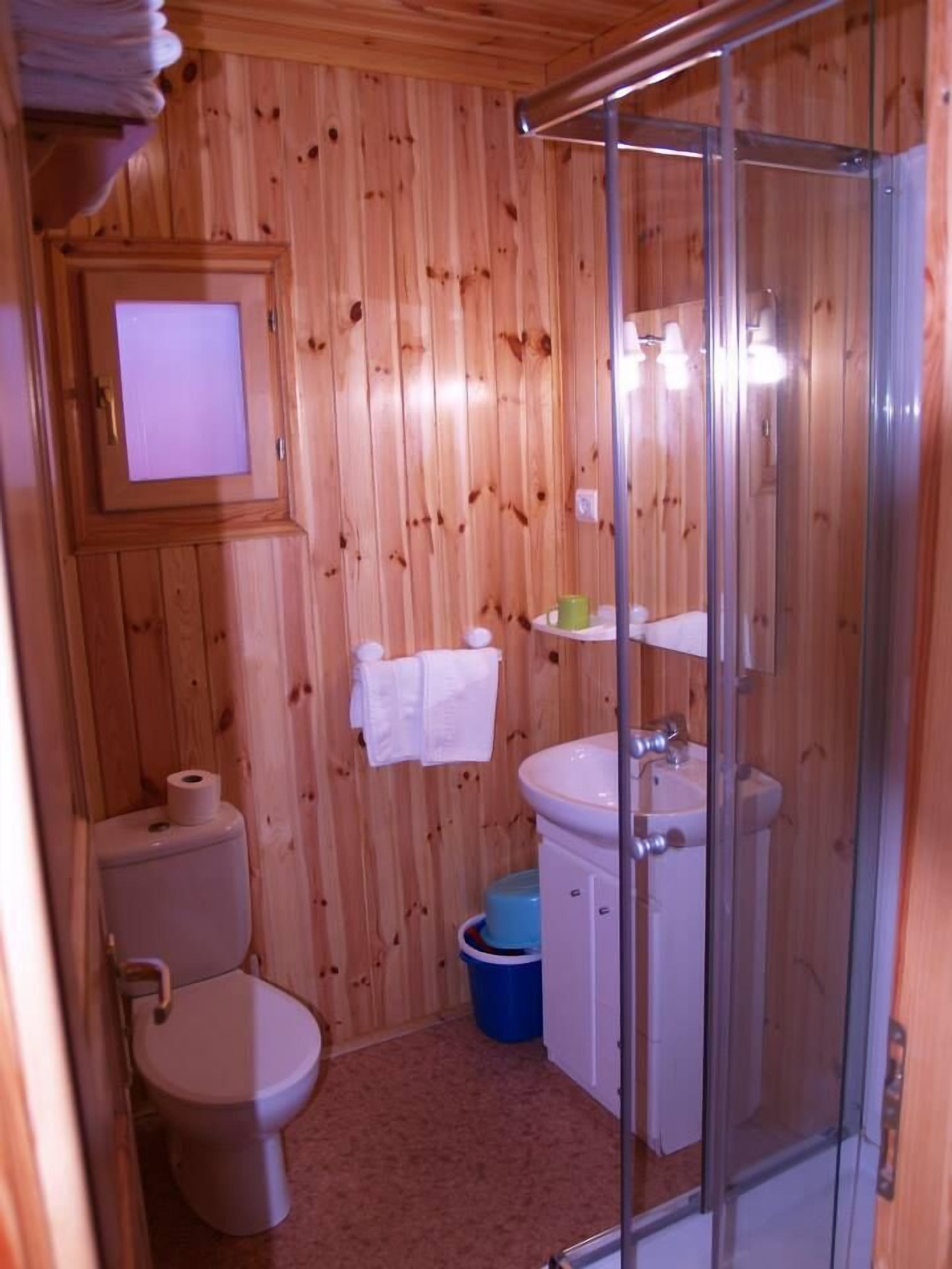 A wooden-paneled bathroom with a toilet, sink, and glass shower enclosure.