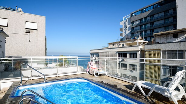 Una piscina en la azotea con vista al océano, rodeada de edificios.