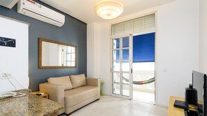 Una sala de estar moderna con un sofá beige, una encimera de granito, un televisor de pantalla plana y un amplio ventanal con vistas a una hamaca al aire libre.