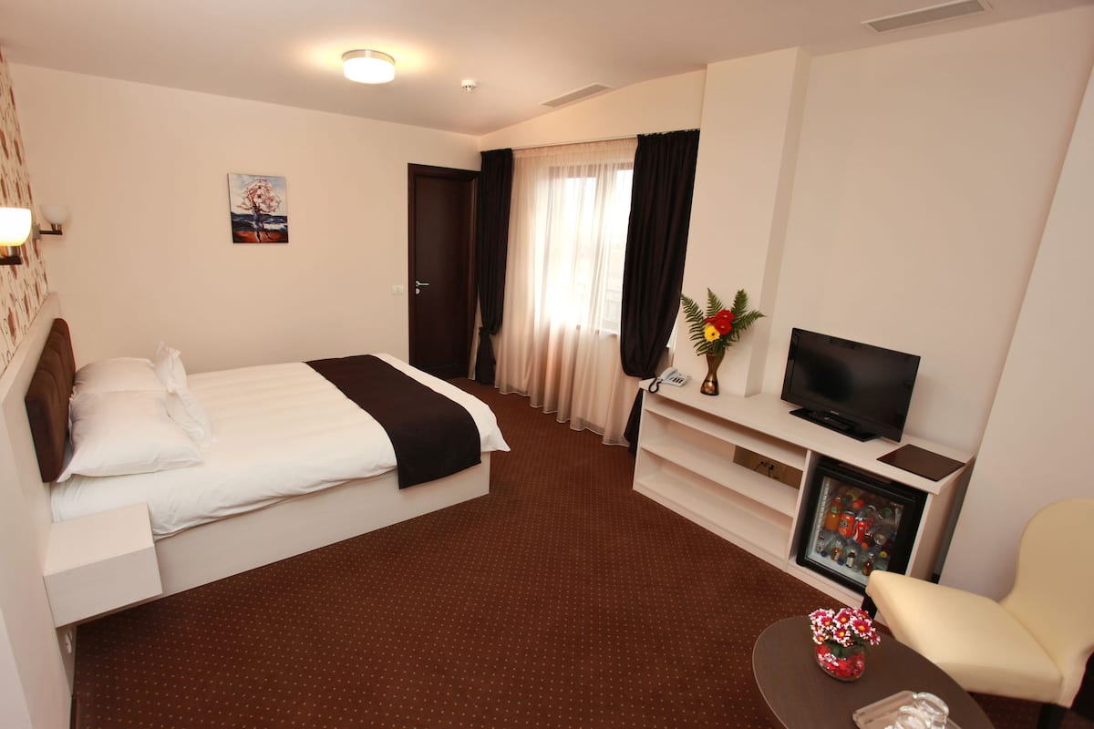 A hotel room with a bed, a TV, a desk, a chair, and a small table with a vase.