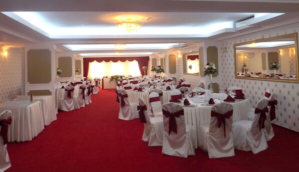 Un salón de banquetes con filas de mesas redondas, manteles blancos y sillas con cintas rojas.