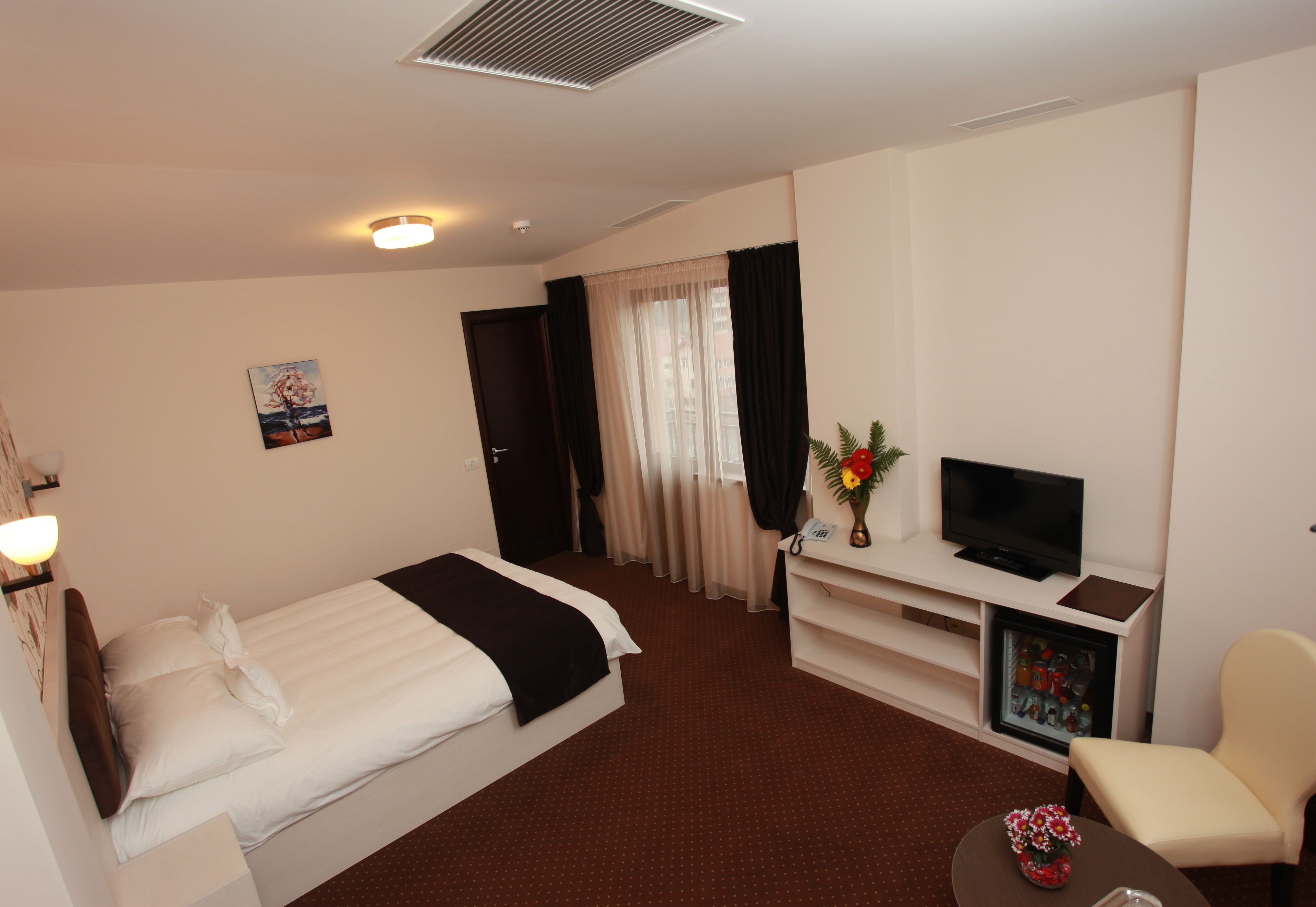 Quarto de hotel com cama, secretária com televisão, cadeira e uma pequena mesa com flores.