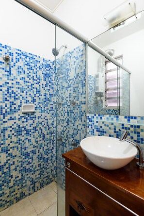 A bathroom with a glass shower enclosure, a white sink, and a tiled wall with blue mosaic tiles. - Omar do Rio - Apartamento SL1004 (Rio de Janeiro)
