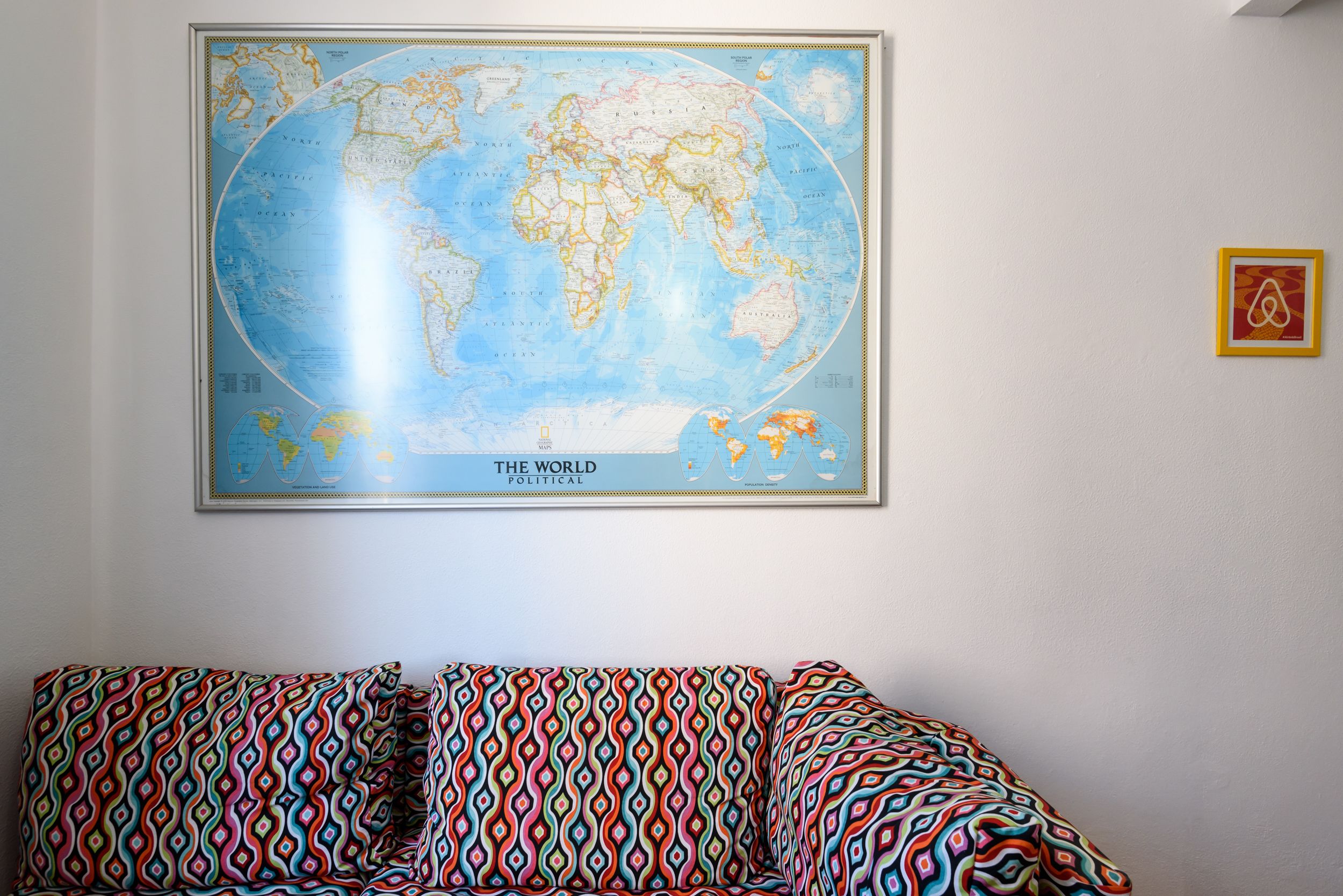 A world map on a wall, a patterned sofa, and a framed picture.