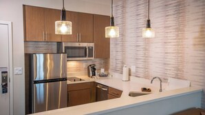 Cozinha moderna com eletrodomésticos de aço inoxidável, armários de madeira e iluminação pendente.