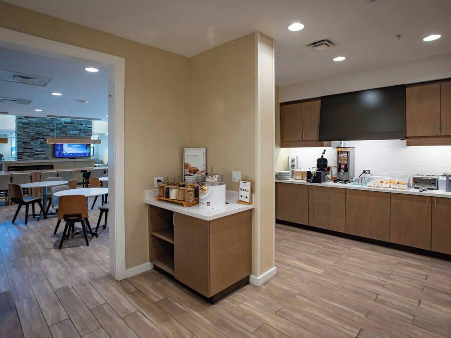 A modern kitchen with wooden cabinets, a central island, and a dining area with chairs and tables.