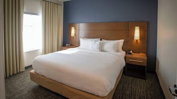 A hotel room with a large bed, two bedside tables with lamps, a window with curtains, and a dark blue accent wall.