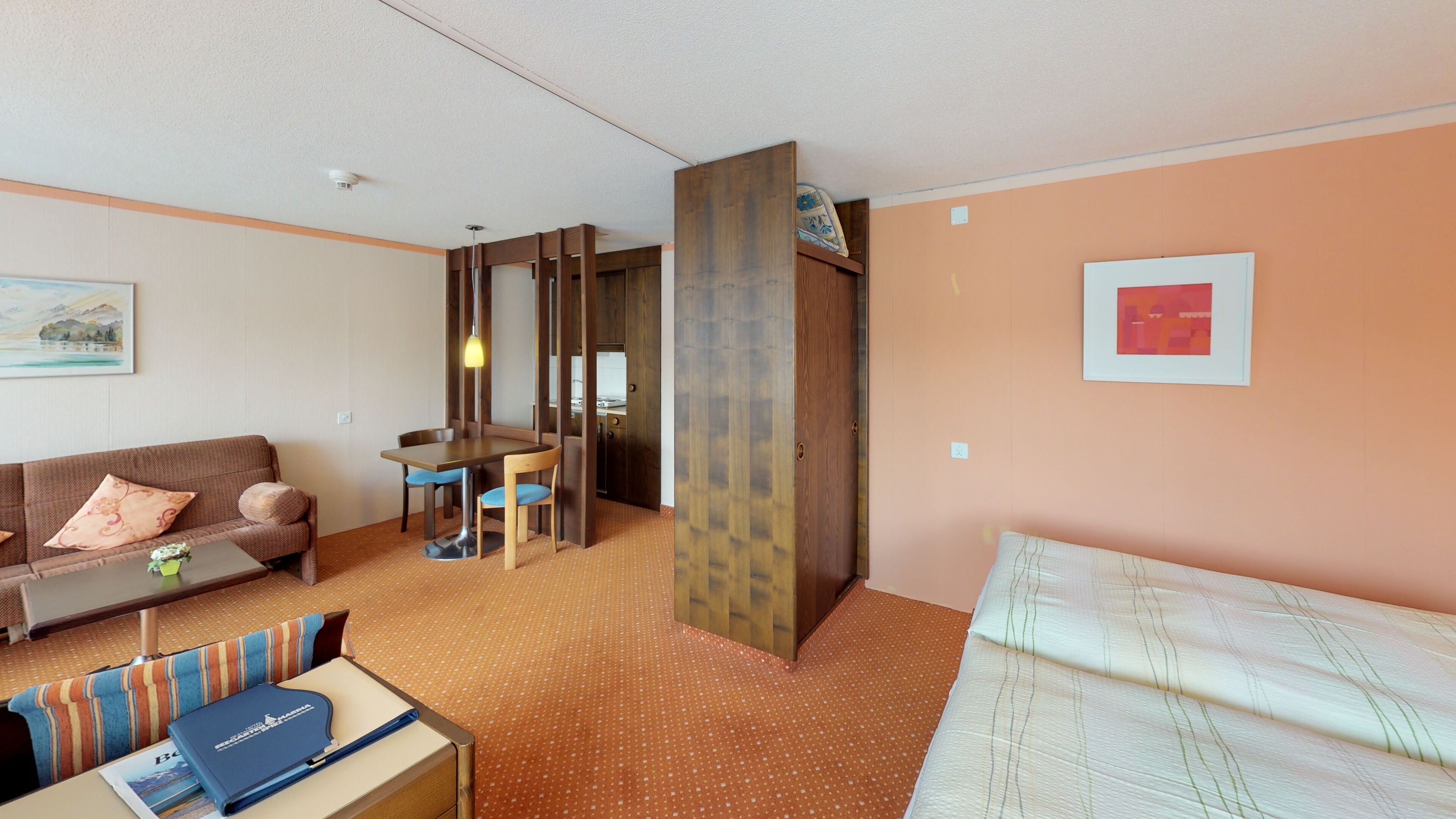 A hotel room with a sofa, a dining table, a small kitchen area, and a bed.
