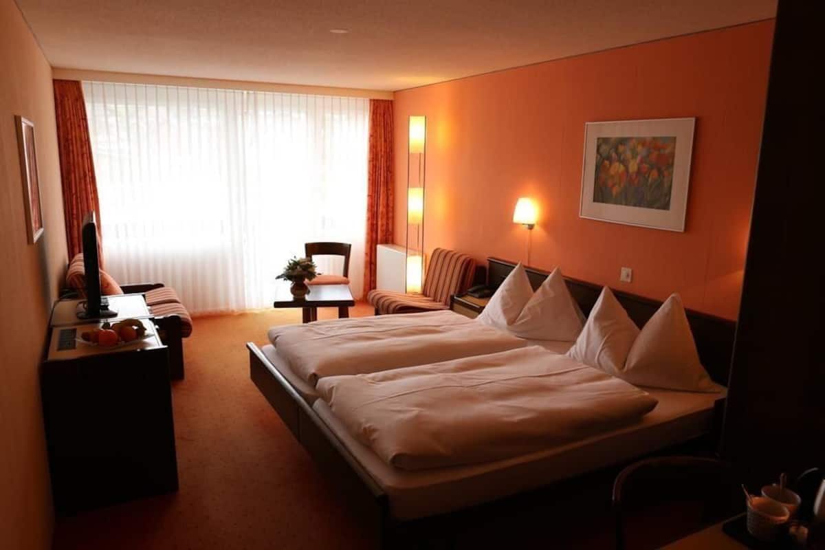 A hotel room with two beds, a desk, a chair, a TV, and a painting on the wall.