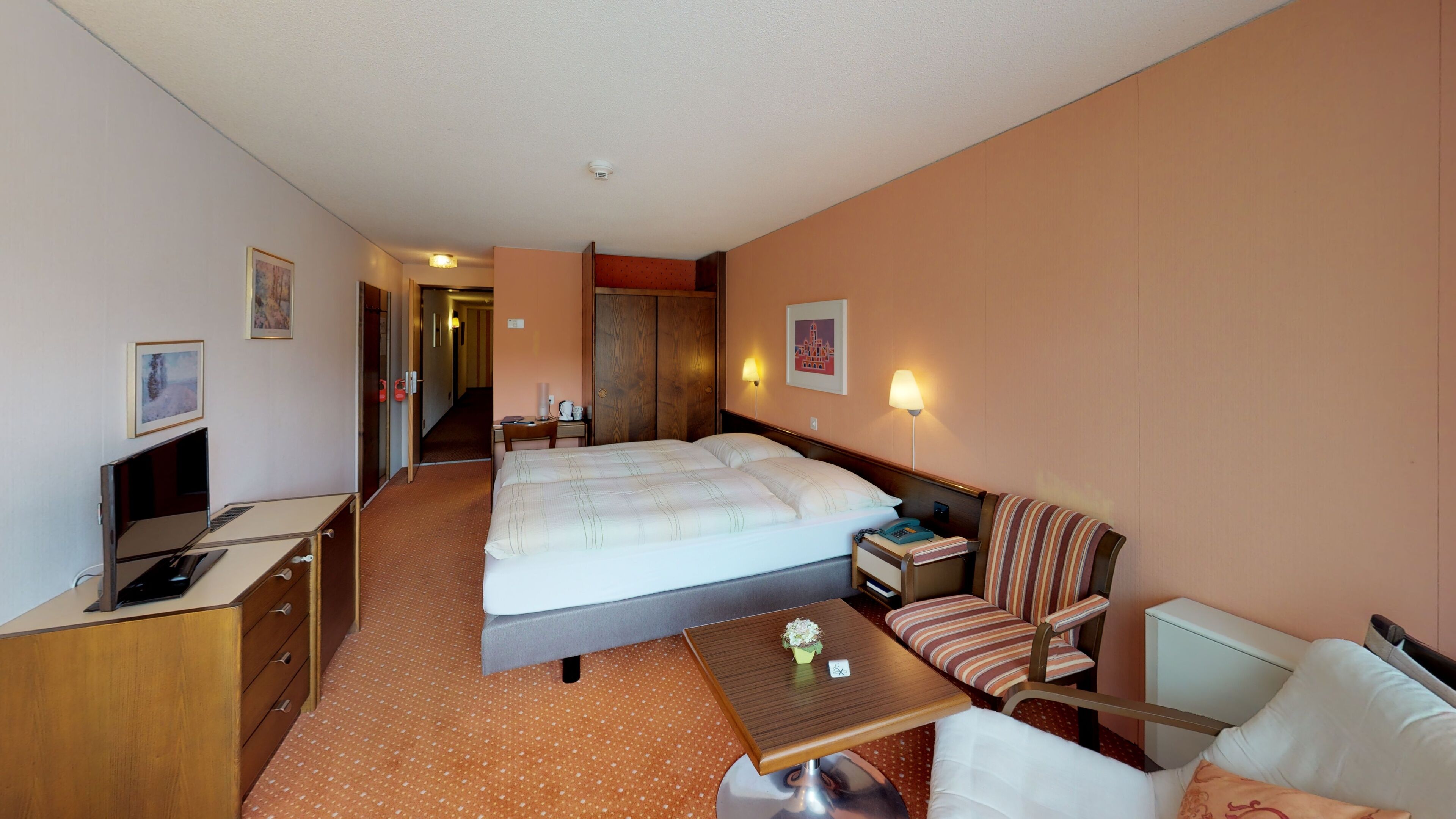 A hotel room with a bed, a desk with a computer, a chair, a small table, and a sofa.