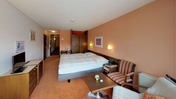 A hotel room with a bed, a desk with a computer, a chair, a small table, and a sofa.