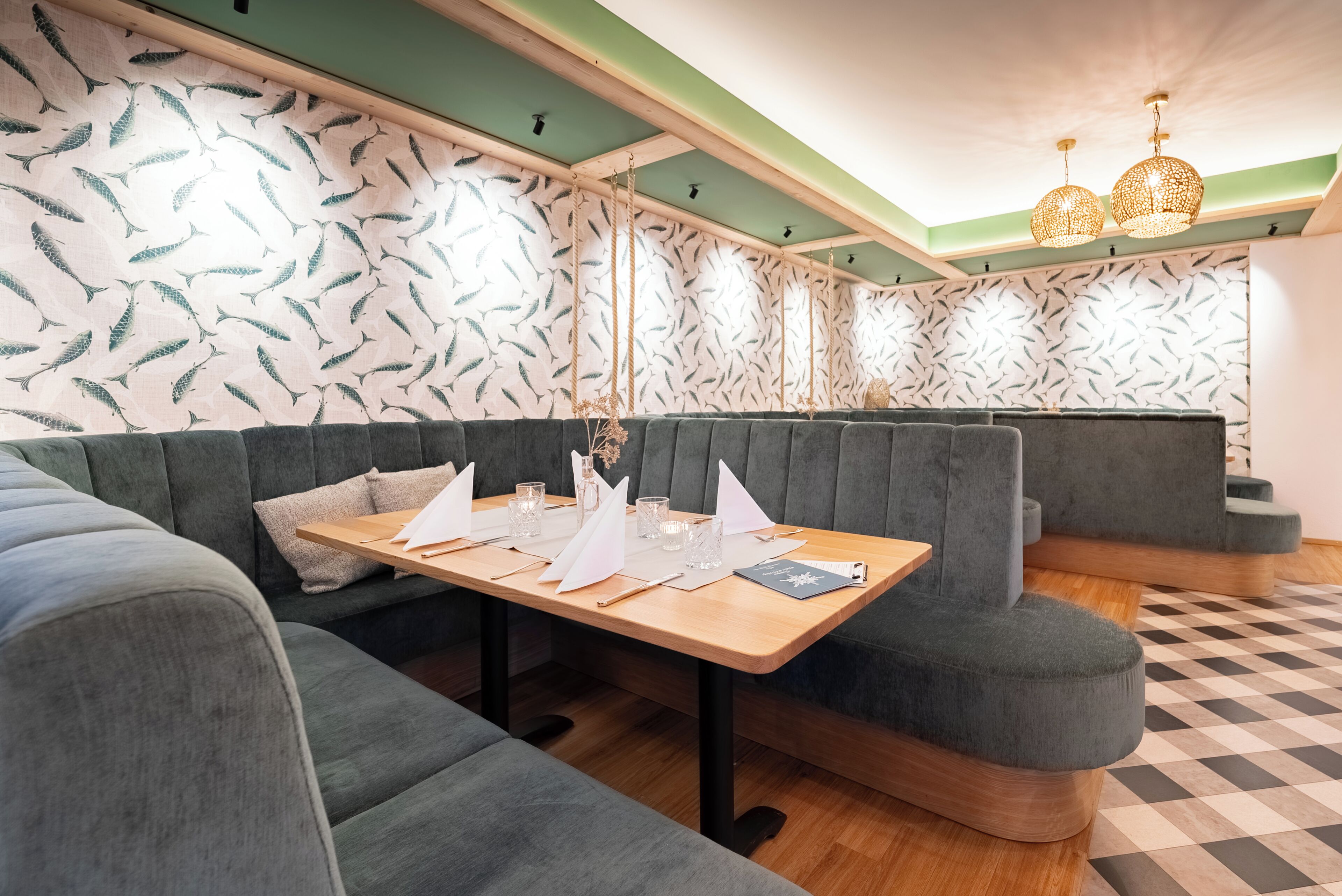 En restaurant med et træbord dækket til spisning, polstrede siddepladser og tapet med mønster.