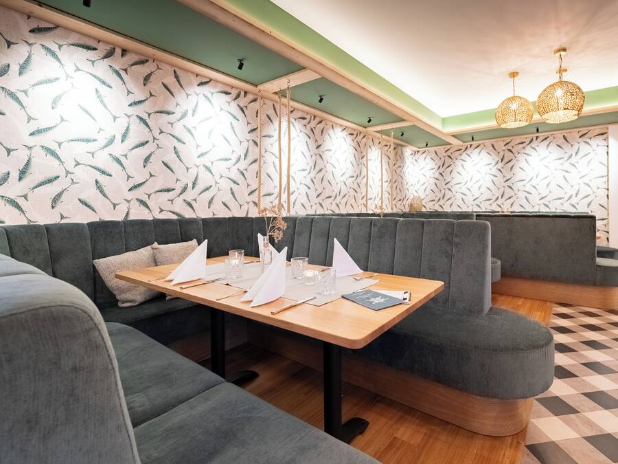 En restaurant med et træbord dækket til spisning, polstrede siddepladser og tapet med mønster.