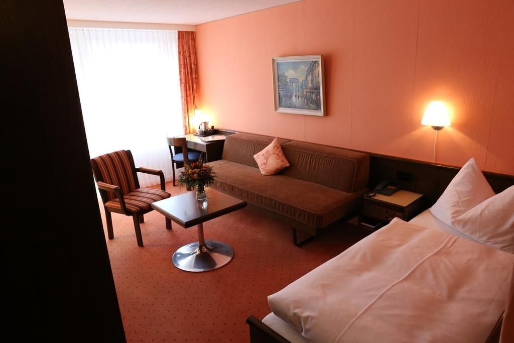 Une chambre d’hôtel avec un lit, un canapé, une table ornée d’un vase de fleurs, une chaise, un bureau et une lampe.