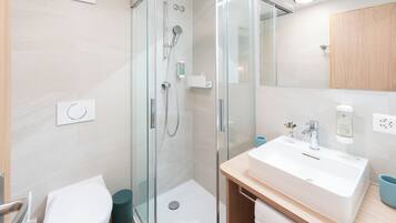 Un baño moderno con cabina de ducha de vidrio, un lavabo blanco y un mueble de tocador de madera.