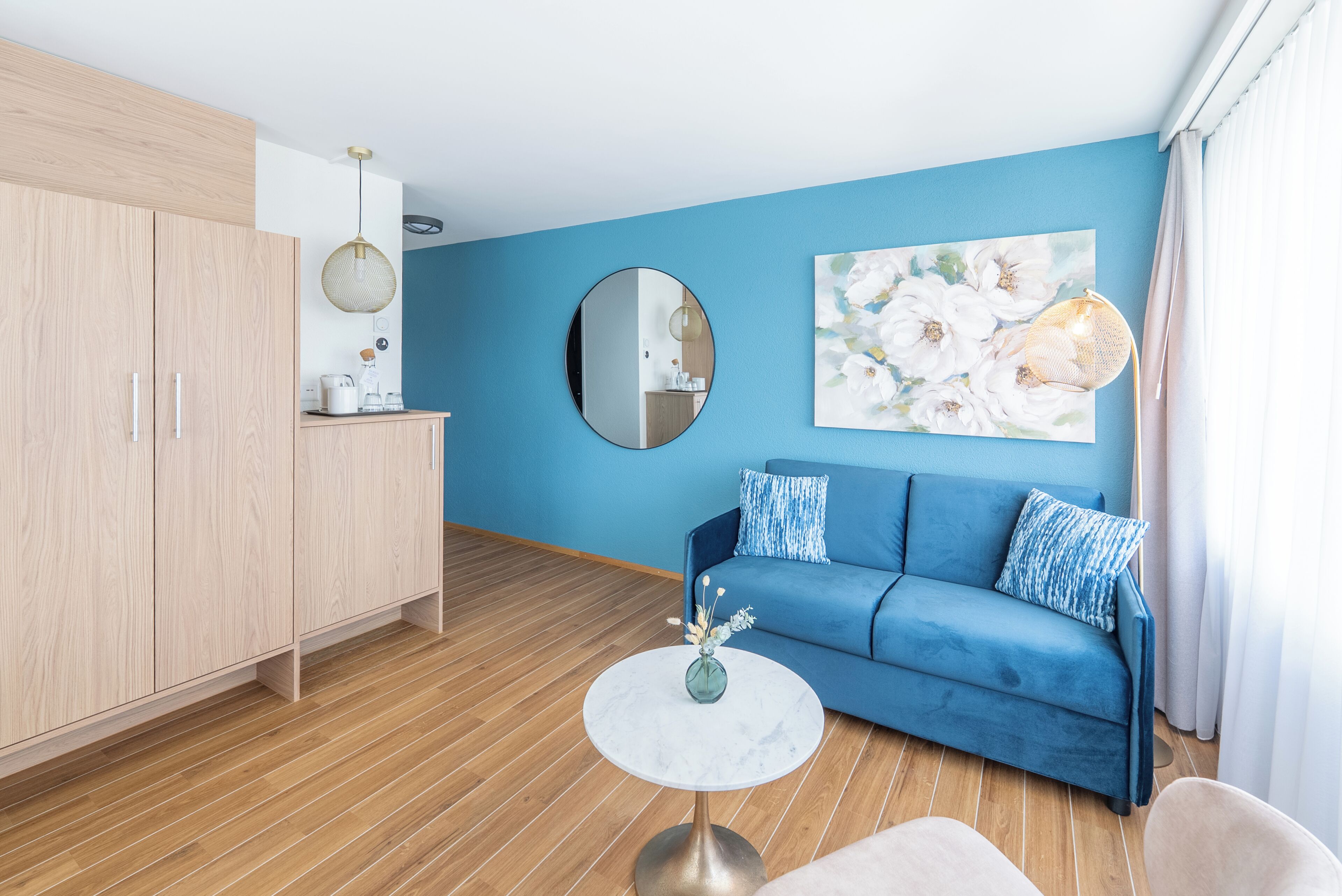 Un salon moderne avec un canapé bleu, un miroir rond et une table basse.