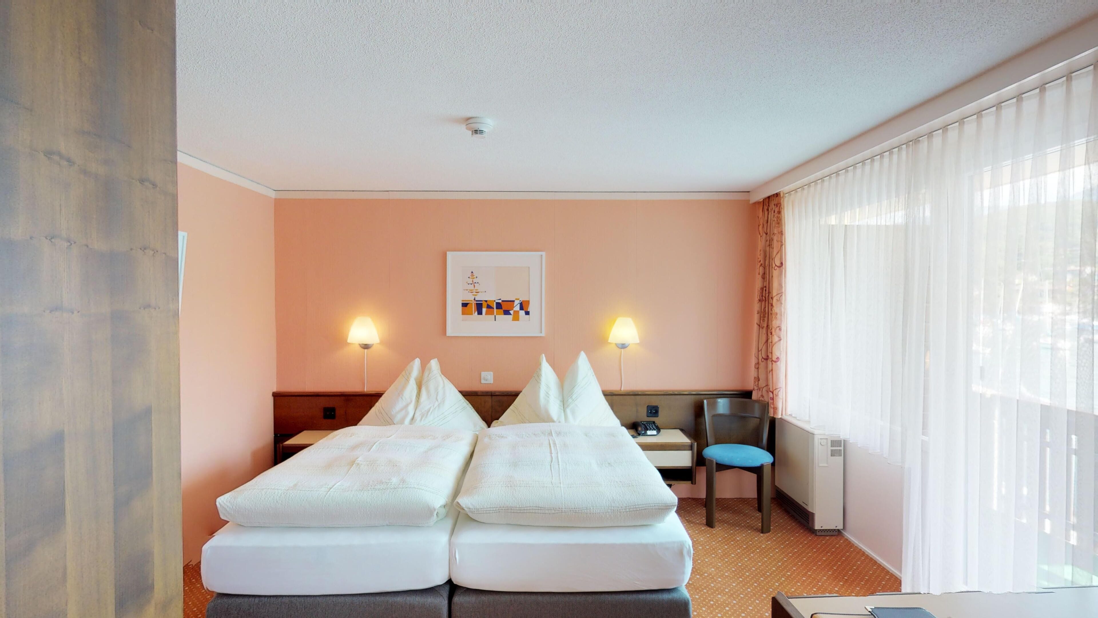 Habitación de hotel con dos camas, un escritorio, una silla, una lámpara y un cuadro en la pared.